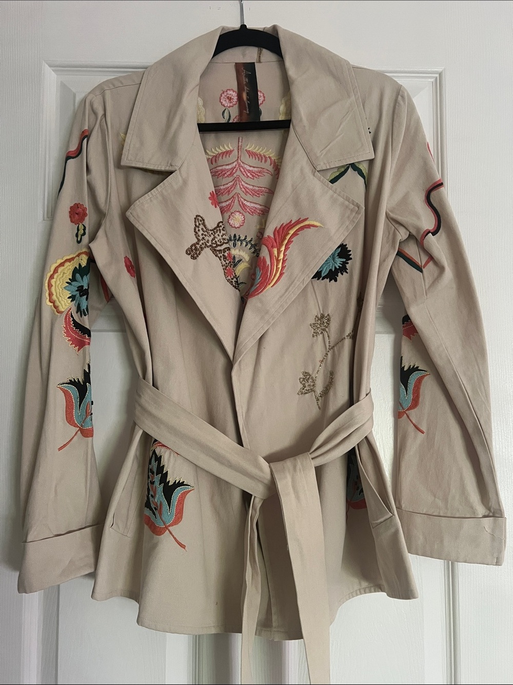 Safari type tan jacket with embroidery and side pockets with tie belt.